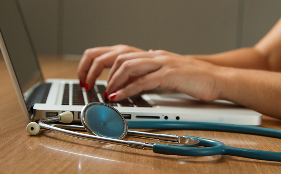 Person typing on laptop with a stethescope