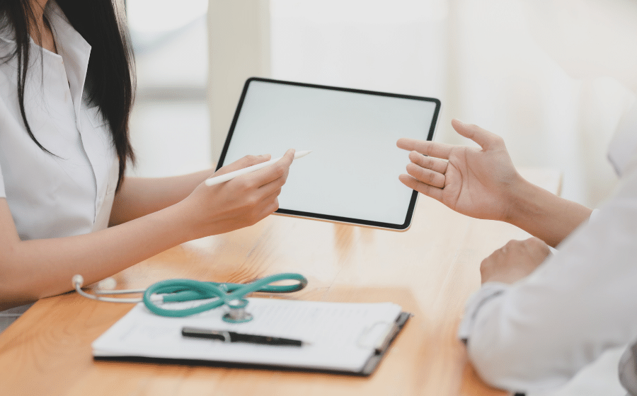 Two people talk over a tablet and stethescope