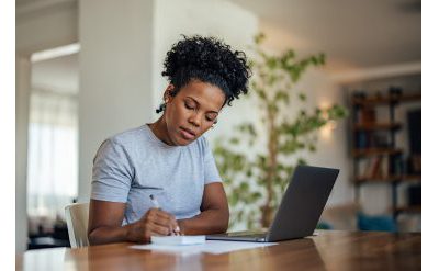 Woman takes notes near laptop