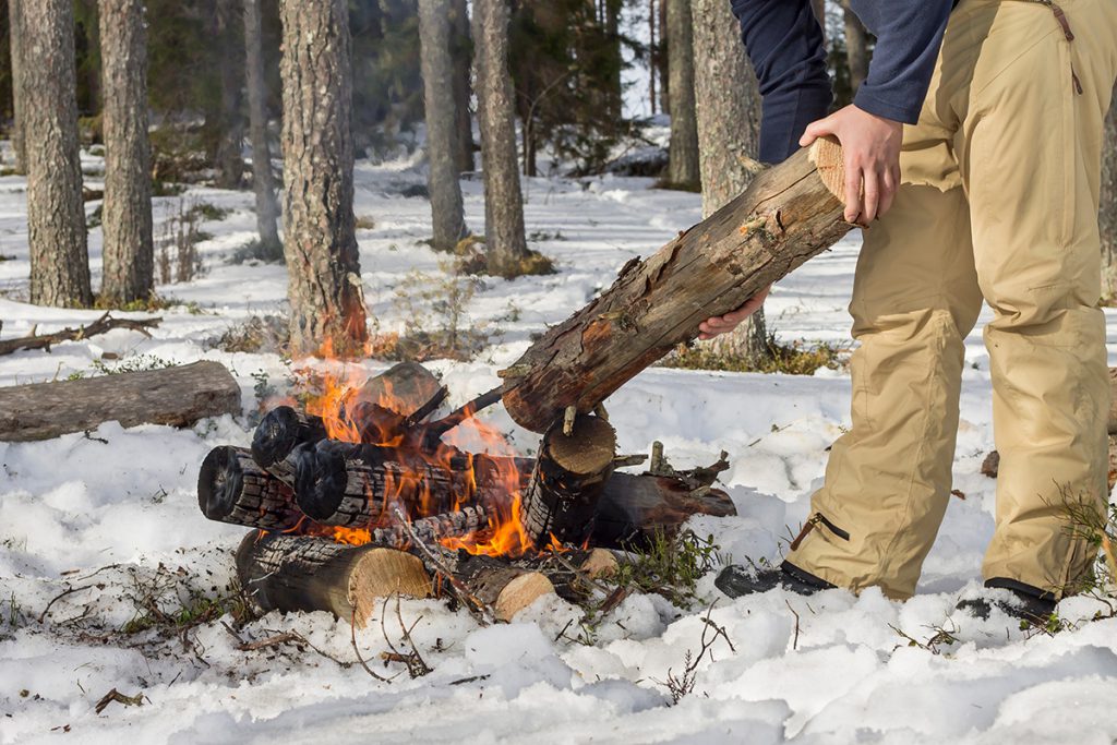 Person adding a log to a fire in the snow